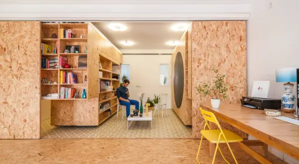 Ein Mann sitzt in einem Raum, der mit OSB-Platten für den Innenausbau gestaltet ist. Bücherregale und ein Schreibtisch sind ebenfalls aus OSB gefertigt.