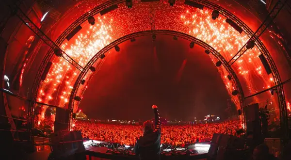DJ z uniesioną pięścią na tle tłumu i fajerwerków. Niezapomniany sunrise lineup na festiwalu.