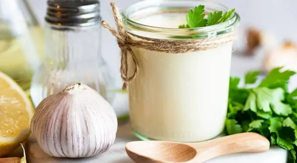 Słoik domowego aioli, czosnek, cytryna i natka pietruszki – składniki idealnego sosu.