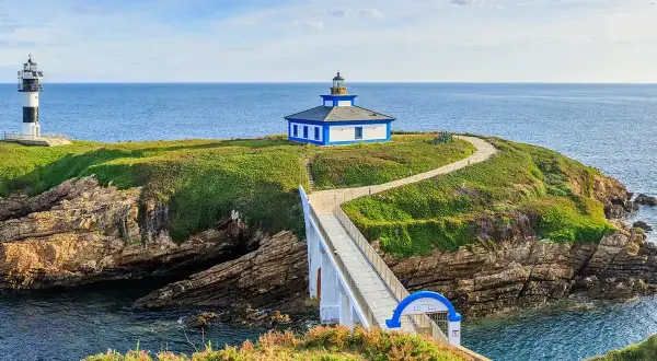 Faro y casa azul en una isla verde, conectada por un puente blanco sobre el mar Cantábrico en Lugo.