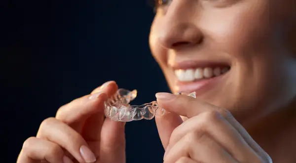 Donna sorridente tiene in mano allineatori dentali trasparenti, pronti per un sorriso perfetto.