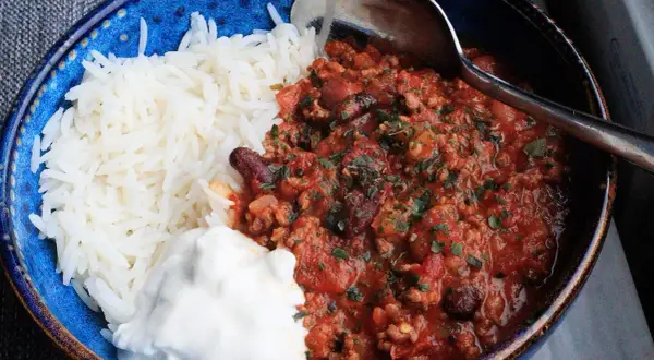 En blå skål med ris, en klick gräddfil och en portion av det godaste chili con carne, toppad med persilja.