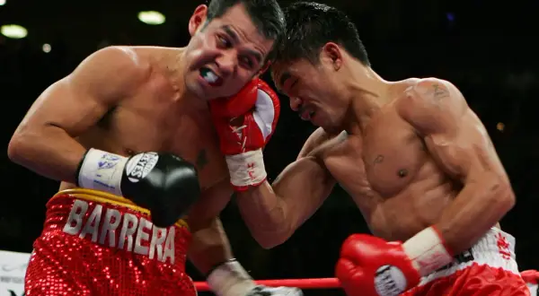 A boxer wearing red shorts with "BARRERA" emblazoned on them takes a hit.