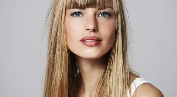 Blonde Frau mit blauen Augen und einem leichten Lächeln. Sie fragt sich, wie oft Haare blondieren für diesen Look nötig ist.