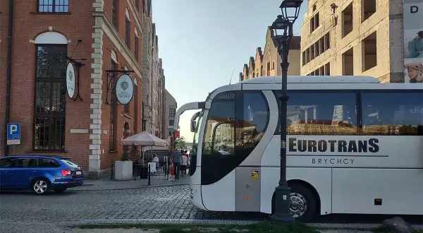 Autobus Eurotrans czeka na pasażerów, którzy zastanawiają się, ile się jedzie do Chorwacji. W tle kamienice i niebieski samochód.