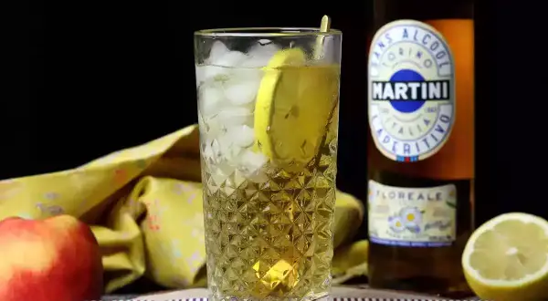 Orzeźwiający Martini Floreale z lodem i cytryną, obok jabłka i butelki Martini.