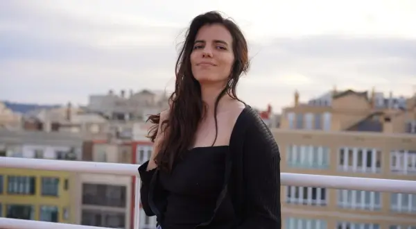 Anna Pazos, con su cabello suelto y una mirada serena, posa en una terraza con edificios de fondo.