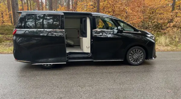 Lexus LM 350h w czarnym kolorze, z otwartymi drzwiami, prezentuje luksusowe wnętrze. Otoczony jesiennym lasem.