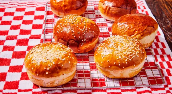 Petits pains à burger dorés et moelleux, certains parsemés de graines de sésame, sur une grille de refroidissement.