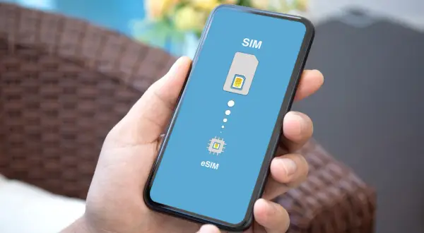 Dłoń trzyma smartfon z ekranem pokazującym porównanie tradycyjnej karty SIM i chipu eSIM. Dowiedz się, esim co to jest.
