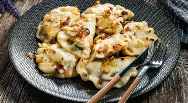 Talerz pełen pysznych, domowych pierogów okraszonych skwarkami. Idealne, gdy zastanawiasz się, ile gotować pierogi, by były miękkie i smaczne.