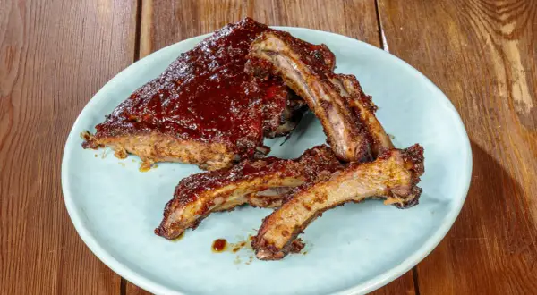 Succulente costine di maiale glassate con salsa barbecue, servite su un piatto azzurro su un tavolo di legno.