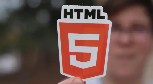 Osoba trzyma naklejkę z logo HTML5, symbolizującą wiedzę, jak utworzyć stronę html.
