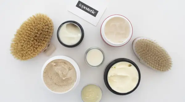 Kremy i peelingi do ciała, szczotki do masażu i wizytówka z napisem "topestetic". Wiele z tych produktów zawiera phenoxyethanol w kosmetykach, zapewniając ich trwałość.