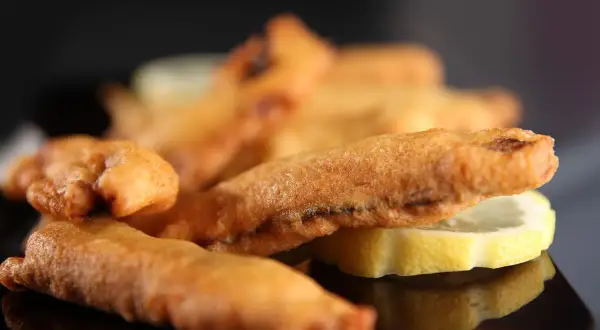 Beignets de sardines dorés et croustillants, servis avec des rondelles de citron sur une assiette noire.