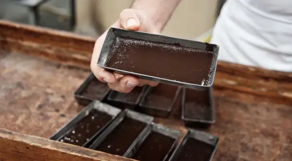 Mani esperte versano cioccolato lavorato a freddo in stampini metallici, pronti per diventare delizie artigianali.
