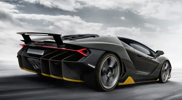 Czarny Lamborghini Centenario z żółtymi akcentami pędzi po drodze, chmury na niebie podkreślają dynamikę.