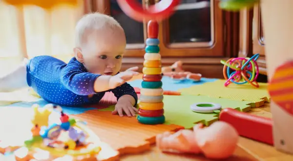 Dziecko bawi się kolorowymi, potencjalnie niebezpiecznymi zabawkami dla dzieci, takimi jak wieża z kółek i spiralna kula.