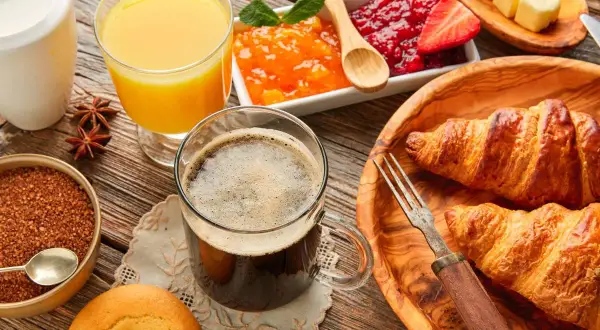 Pyszne śniadanie kontynentalne: świeże croissanty, dżemy, masło, kawa i sok pomarańczowy na drewnianym stole.