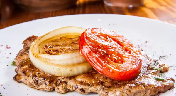 Karkówka pieczona w plastrach z cebulą i pomidorem. Aromatyczne danie, które zachwyci każdego smakosza.