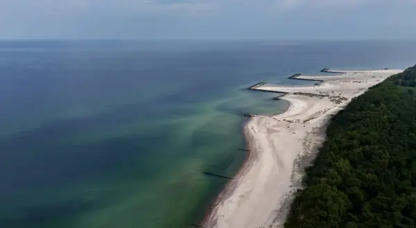 Plaża w Jarosławcu, zwana czasem "plażą dubaj", z kamiennymi falochronami i zielonym lasem.