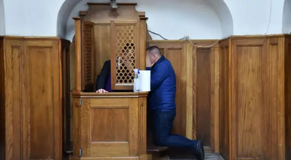 Mężczyzna klęczy przy konfesjonale, zasłaniając twarz. Czy w kościele anglikańskim jest spowiedź?