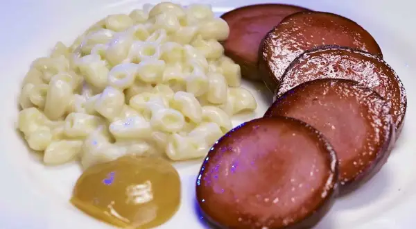 En tallrik med stuvade makaroner, skivad falukorv och en klick senap. En snabb och klassisk svensk måltid.