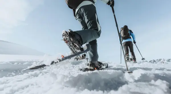 Deux personnes font une randonnée dans la neige, leurs raquettes s'enfonçant dans la poudreuse. Le ciel bleu clair promet une belle journée d'aventure.