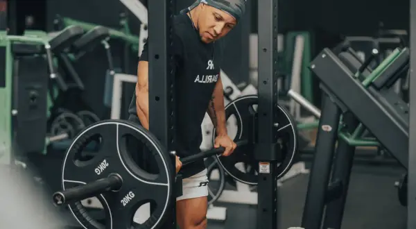 Mann mit Bandana macht schwere myo reps mit Langhantel im Fitnessstudio.