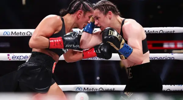 Two professional female boxers clash heads in the ring, their faces intense as they block punches.