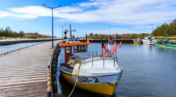 Port w Dźwirzynie, z łodzią rybacką przy drewnianym pomoście, zaprasza na morskie przygody. Atrakcje czekają!