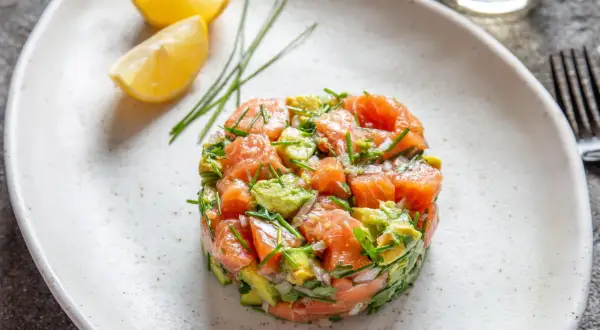 Un délicieux tartare de saumon frais, mélangé à de l'avocat et des herbes, servi avec des quartiers de citron.