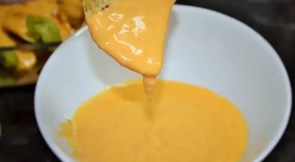 Un totopo cubierto de queso fundido cremoso se sumerge en un tazón de queso.