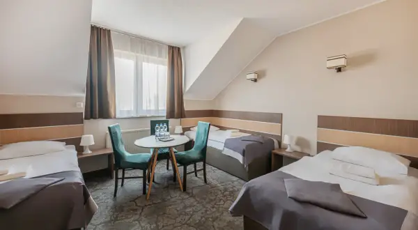 Pokój hotelowy z trzema łóżkami, stolikiem i krzesłami.
