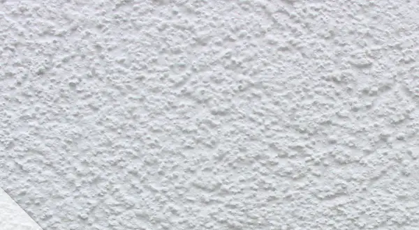 Nahaufnahme einer weißen, strukturierten Wand, die zeigt, wie man eine Wand verputzt. Das Korn ist unregelmäßig und erzeugt eine interessante Textur.