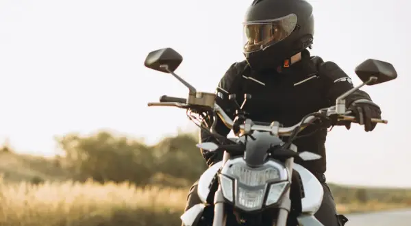Motocyklista w kasku i kurtce siedzi na motocyklu na tle krajobrazu.