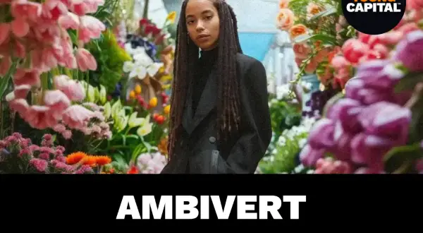 Een jonge vrouw met vlechten staat tussen bloemen. De tekst "AMBivert" suggereert de betekenis van ambivert: iemand die zowel extravert als introvert is.