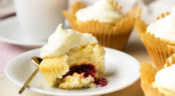 En närbild på en cupcake med vit frosting och en härlig röd fyllning. Flera liknande cupcakes med fyllning syns i bakgrunden.