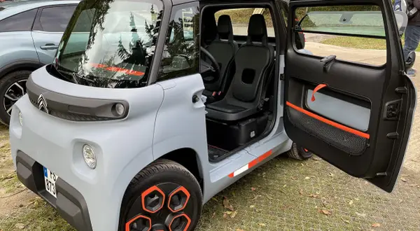 Citroën Ami, un quadriciclo elettrico compatto, con porte aperte e interni visibili. Il suo design unico e le dimensioni ridotte lo rendono perfetto per la città.