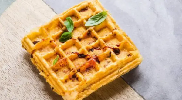 Goldbraune belgische Waffeln mit dunklem Sirup und frischem Basilikum, serviert auf einem Holzbrett.