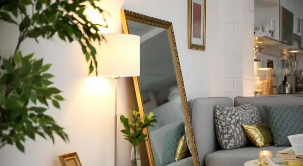 Ein großer Spiegel und eine Stehlampe helfen, die dunkle Wohnung heller zu machen. Ein Sofa mit Kissen und eine Pflanze vervollständigen die Szene.