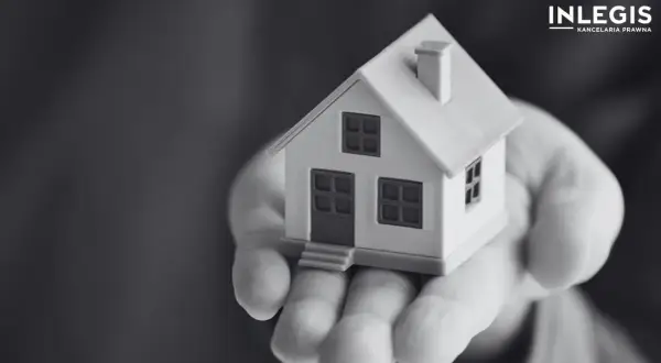 Miniatura domu na dłoni, symbolizująca ograniczone prawa rzeczowe i bezpieczeństwo posiadania.