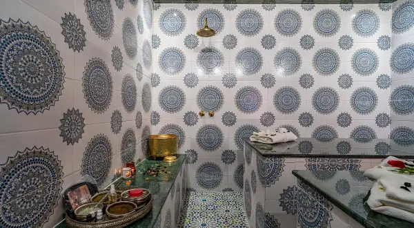 Ett vackert hammam i Marrakech med traditionella mönster på väggarna och golvet. En gyllene skål och skönhetsprodukter står redo för en avkopplande upplevelse.
