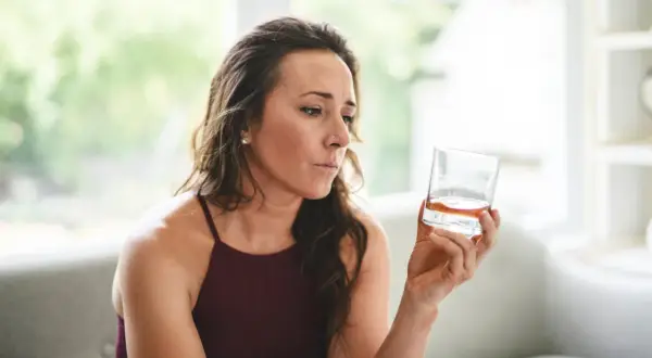 Kobieta zamyślona trzyma szklankę z bursztynowym płynem. Czy to izotek, czy alkohol?