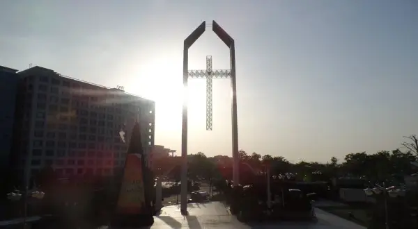Ein monumentales Kreuz ragt im Gegenlicht empor, ein Symbol der Hoffnung, das mit dem Erbe von David Yonggi Cho verbunden ist.
