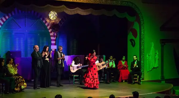 Una bailarina de **tango flamenco** con un vestido rojo y lunares negros cautiva en el escenario, acompañada por guitarristas y cantantes.