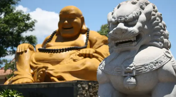 Złoty Budda i kamienna lwica strażniczka na tle błękitnego nieba.