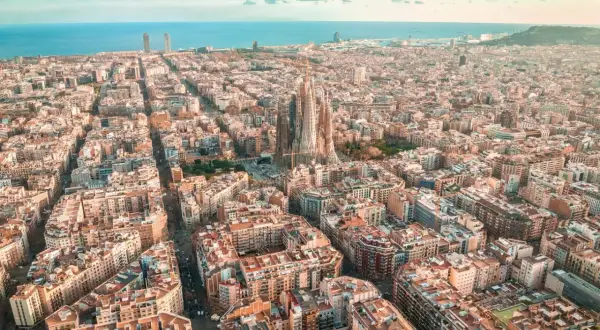 Widok z lotu ptaka na Eixample w Barcelonie, z Sagradą Familią górującą nad miastem i morzem w tle.