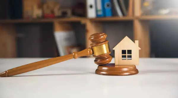 Richterhammer und Holzhaus-Modell auf einem Tisch, symbolisch für ein Immobilien-Bieterverfahren.