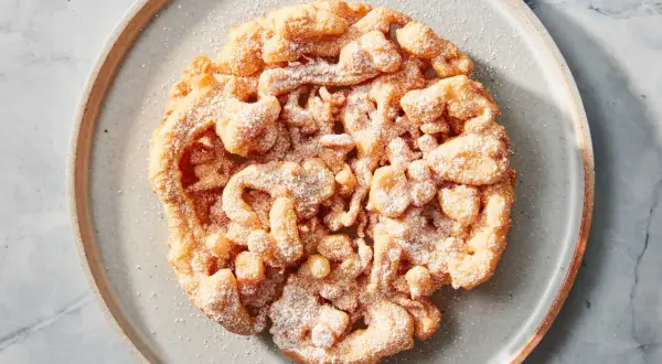 Ein goldbrauner, puderzuckerbestäubter **Funnel Cake** auf einem grauen Teller.